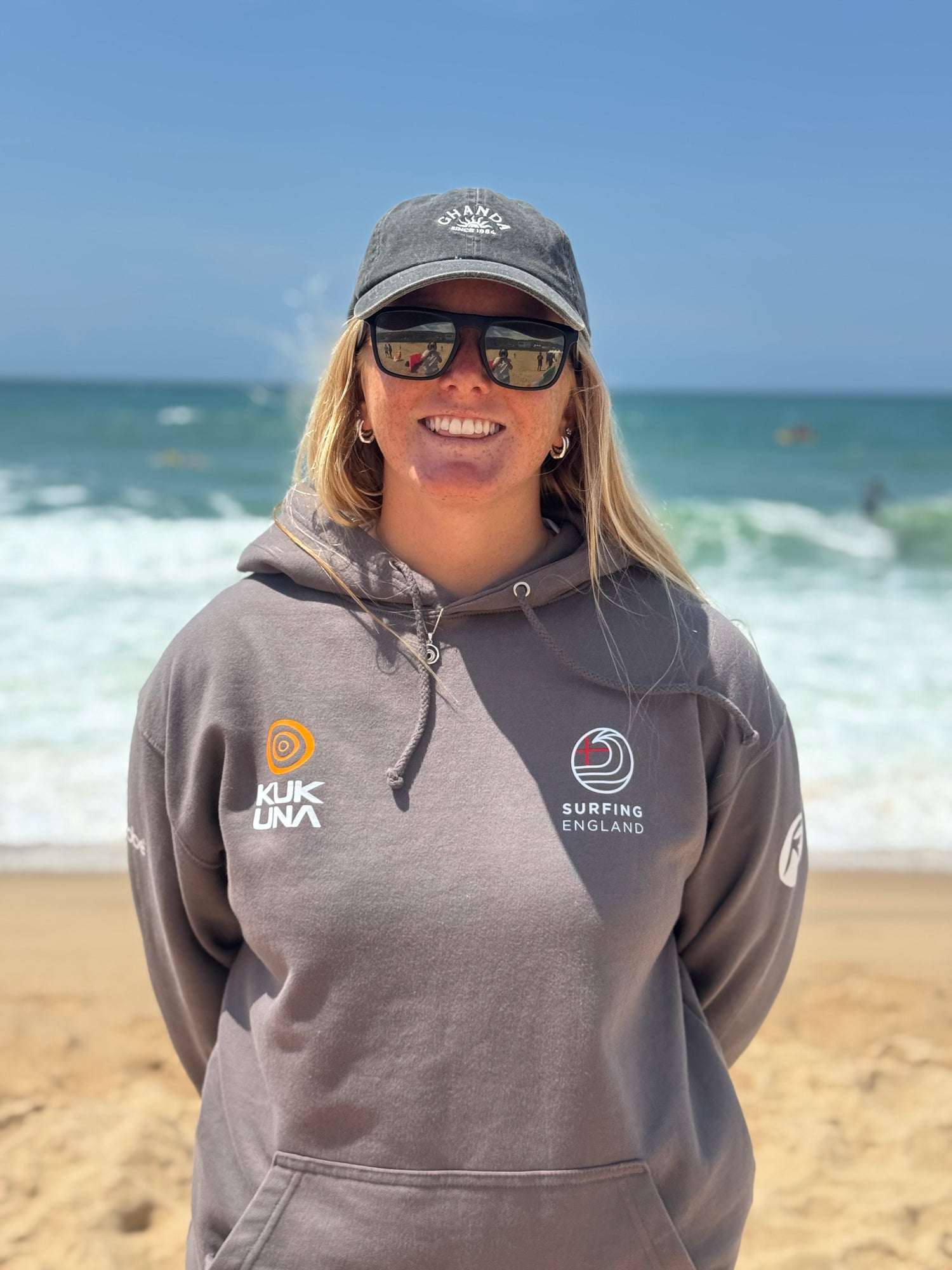 Charlotte Mulley, pro surfer wearing a grey hoodie with logos on a beach