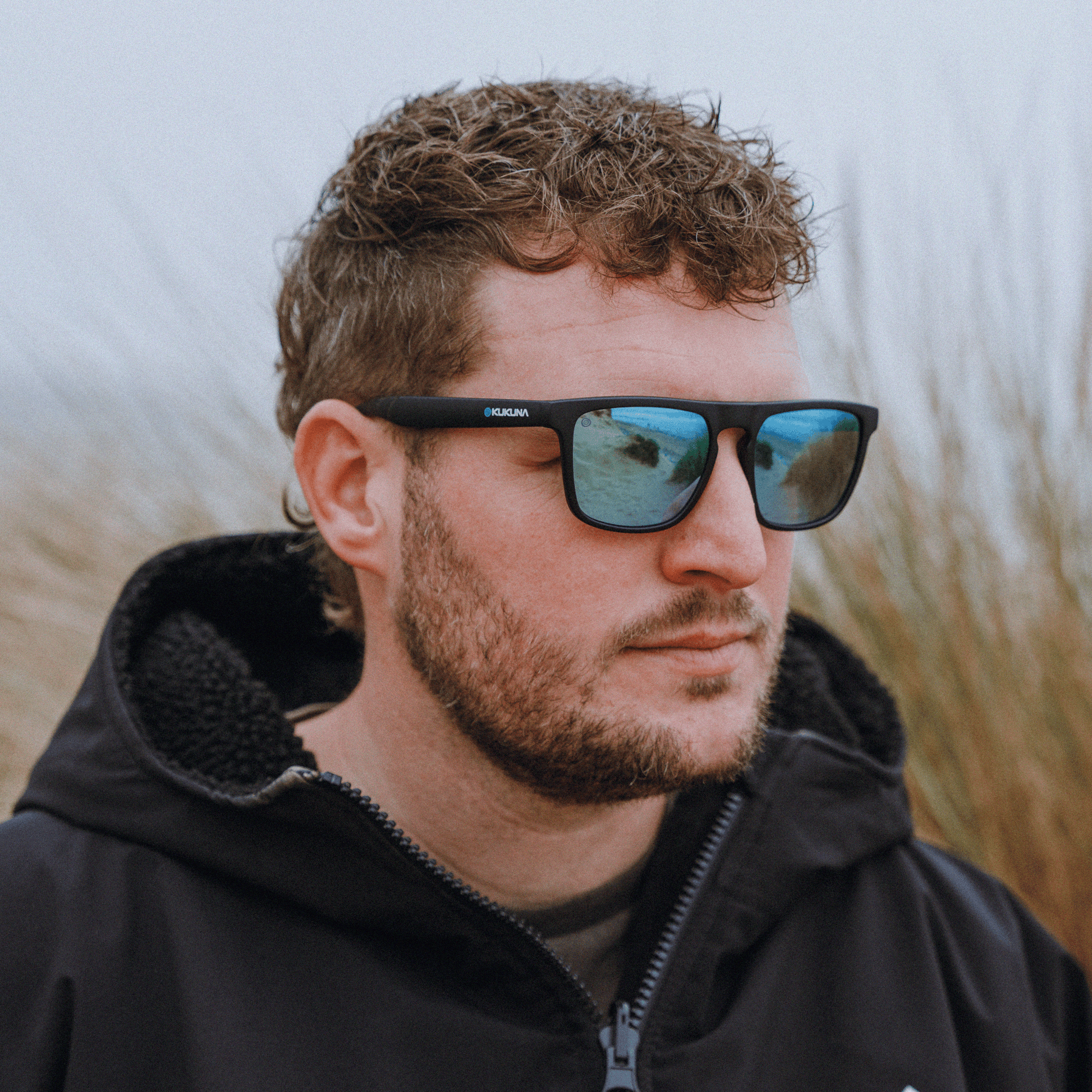 Kukuna® Barricane lifestyle sunglasses on a man with a grey lens and blue mirror, featuring a matte black TR90 frame.