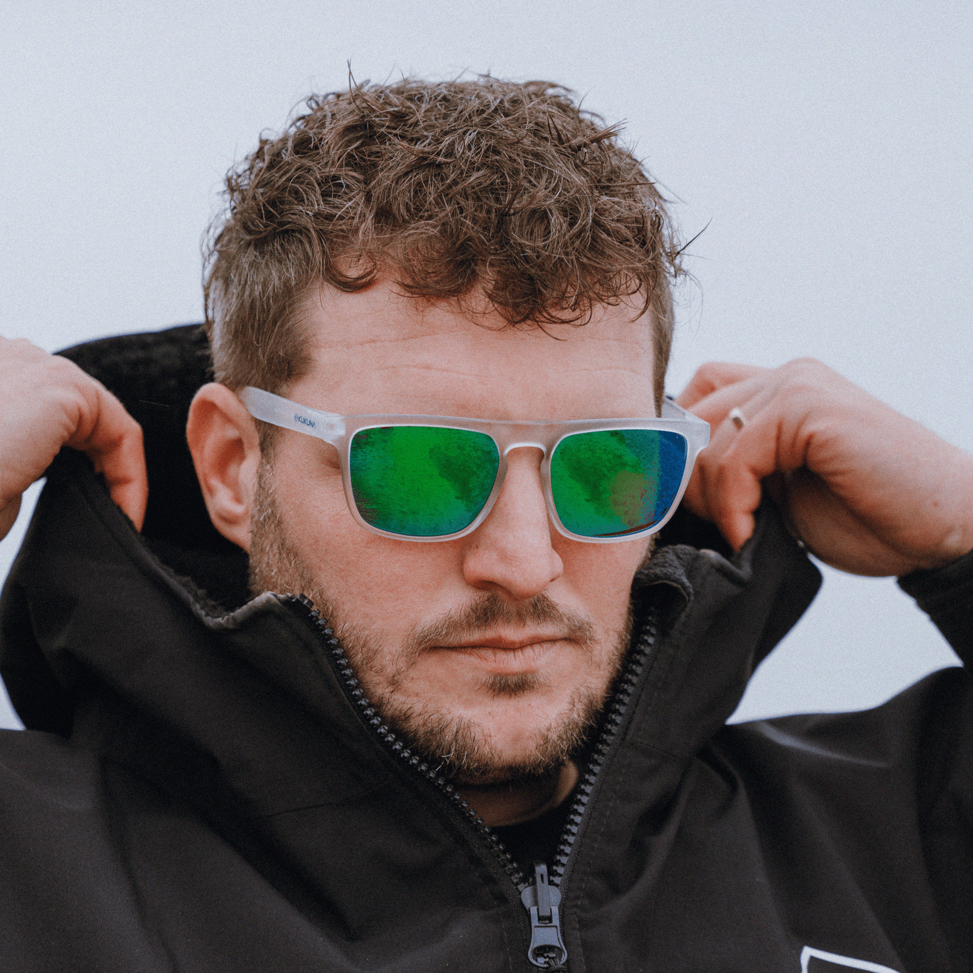 male surfer wearing  Kukuna Barricane polarised sunglasses with clear frosted frame and green mirror lenses