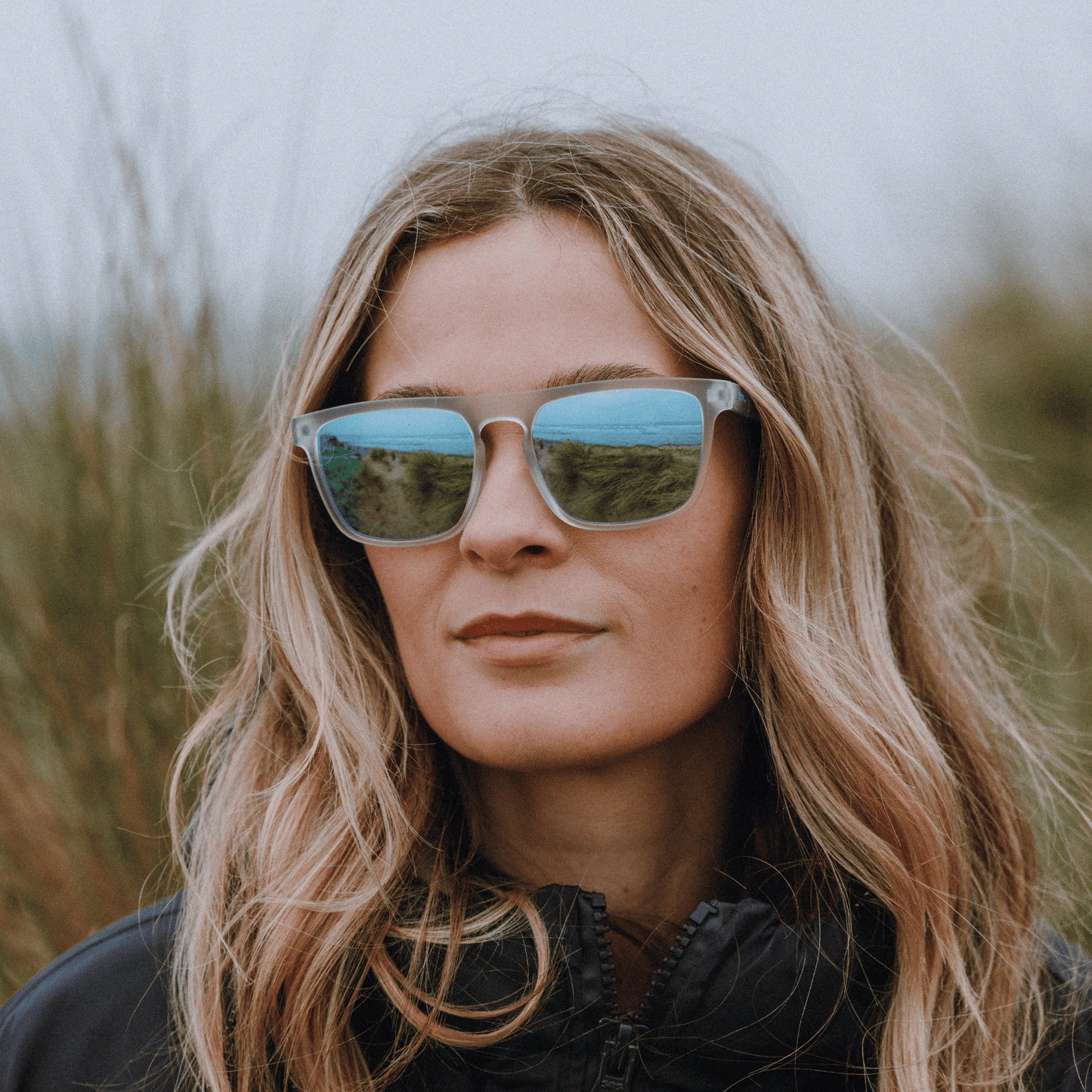 Female surfer wearing Kukuna Barricane durable sports glasses with clear frosted frame and blue mirror lenses