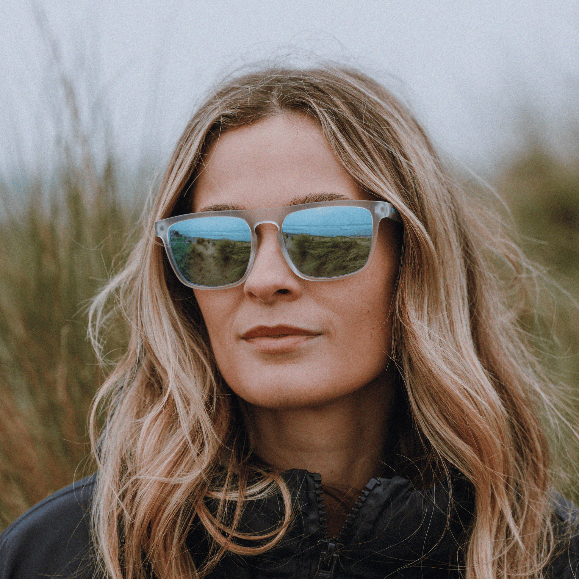 Female surfer wearing Kukuna Barricane durable sports glasses with clear frosted frame and blue mirror lenses