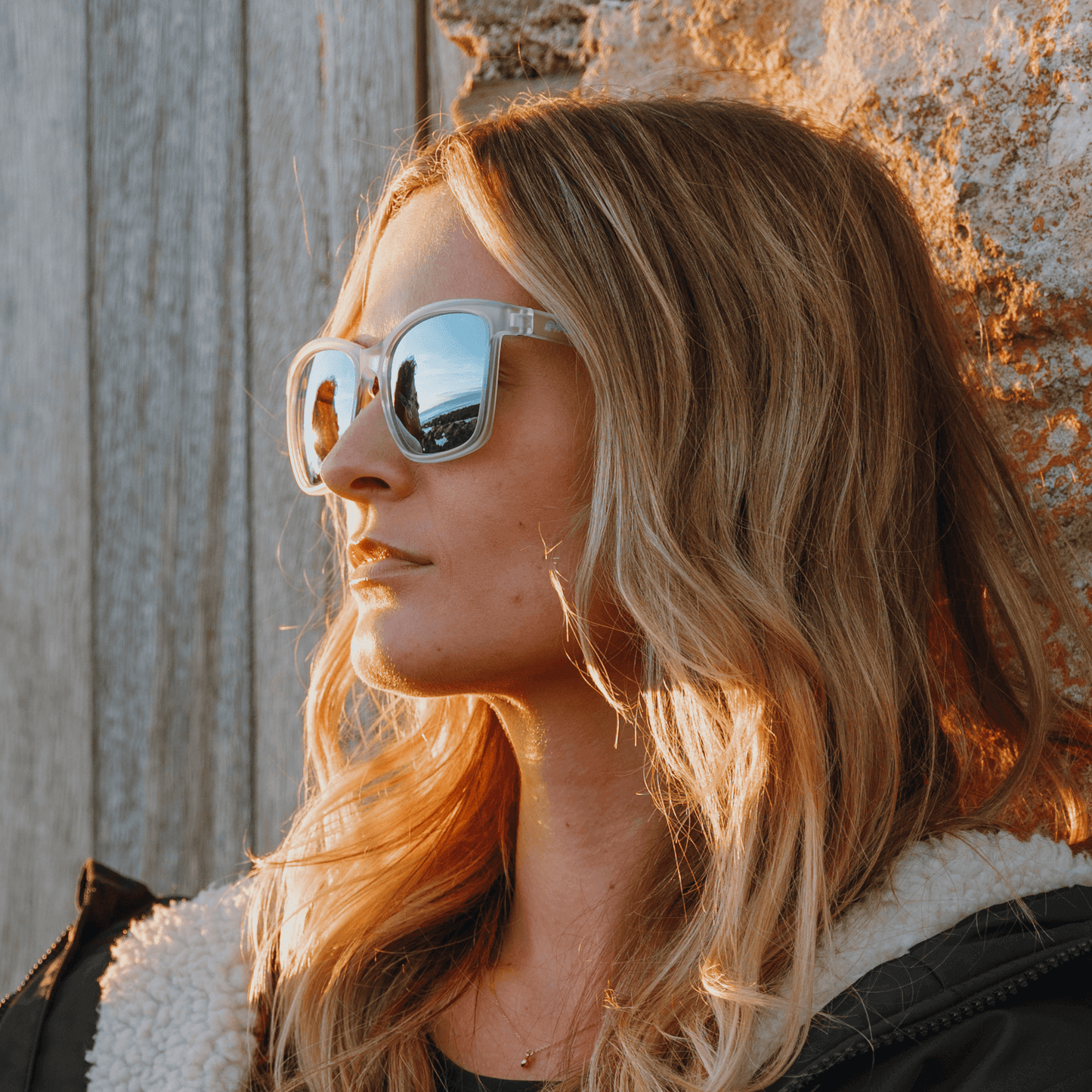 Woman wearing Kukuna® Nanjizal lifestyle sunglasses with clear frosted frame and blue mirror lenses.