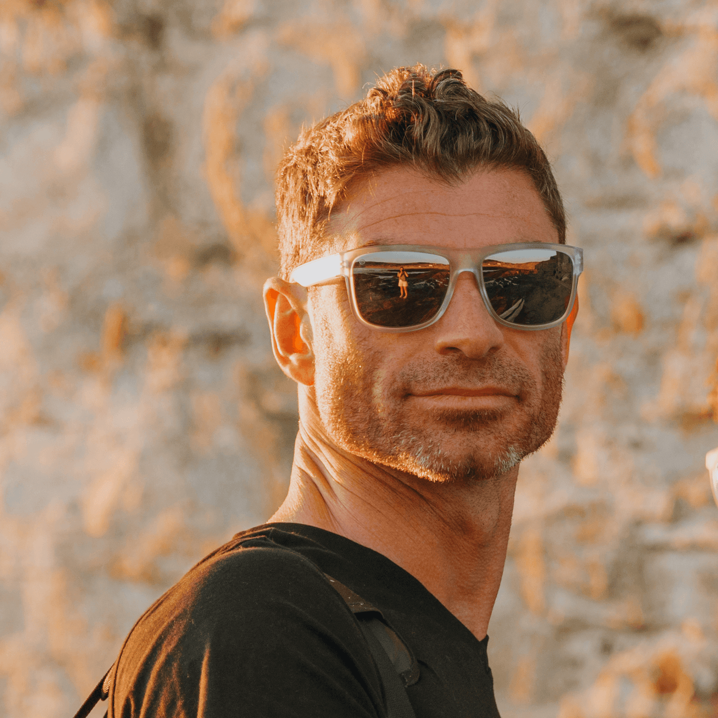 Man wearing Kukuna® Nanjizal lifestyle sunglasses with clear frosted frame and grey lenses, stylish look in outdoor setting.