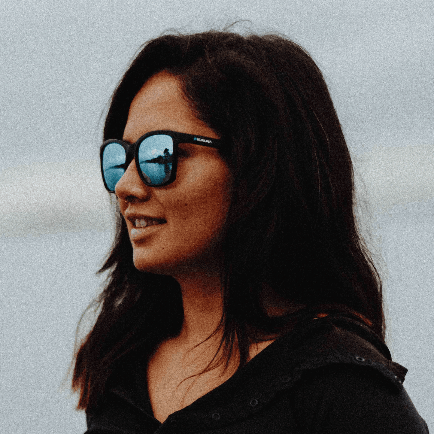 Woman wearing Kukuna® Seaton lifestyle sunglasses with blue mirror lens and matt black TR90 frame, enjoying the outdoors.
