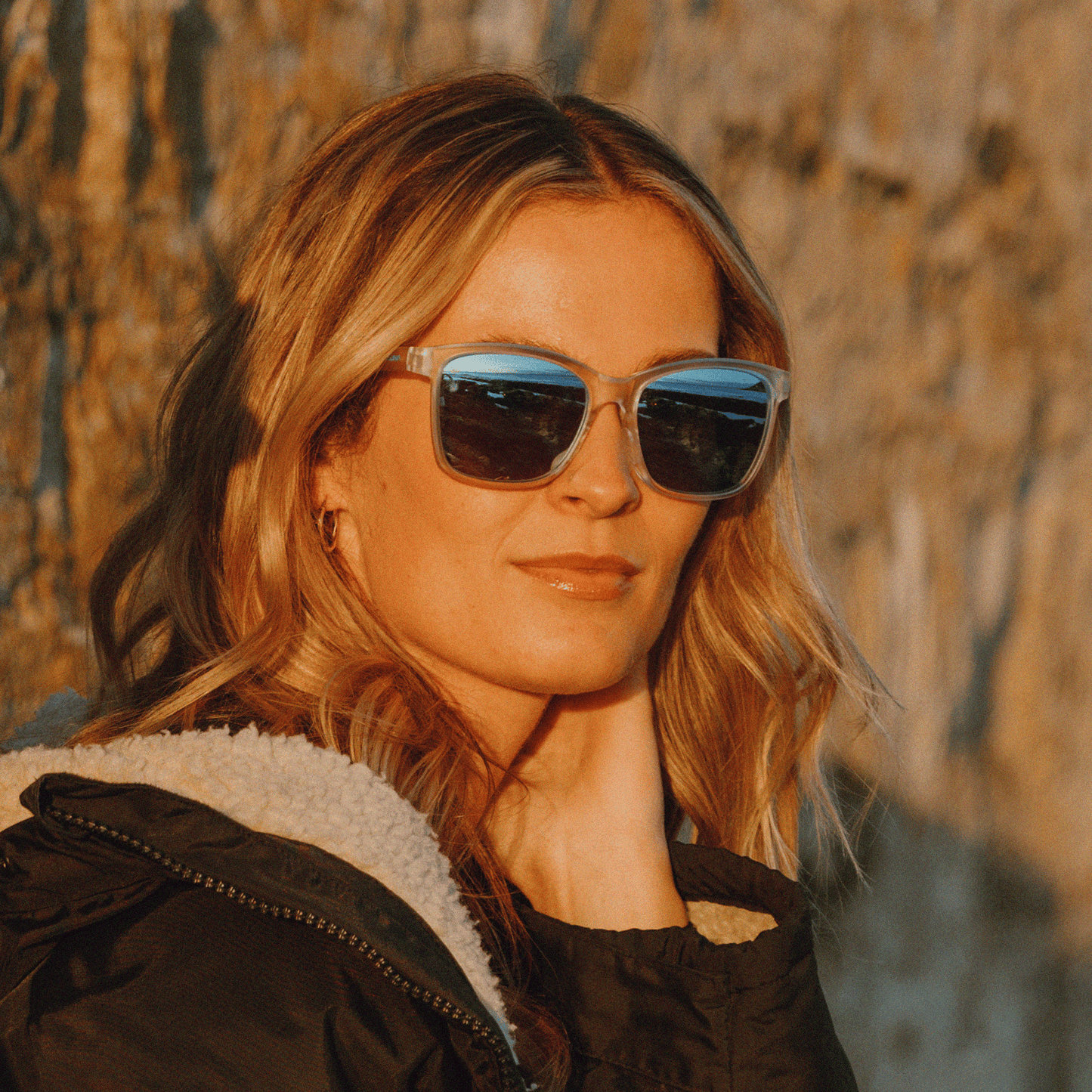 Woman wearing Kukuna Seaton lifestyle sunglasses with grey lens and blue mirror, posed outdoors in golden light.