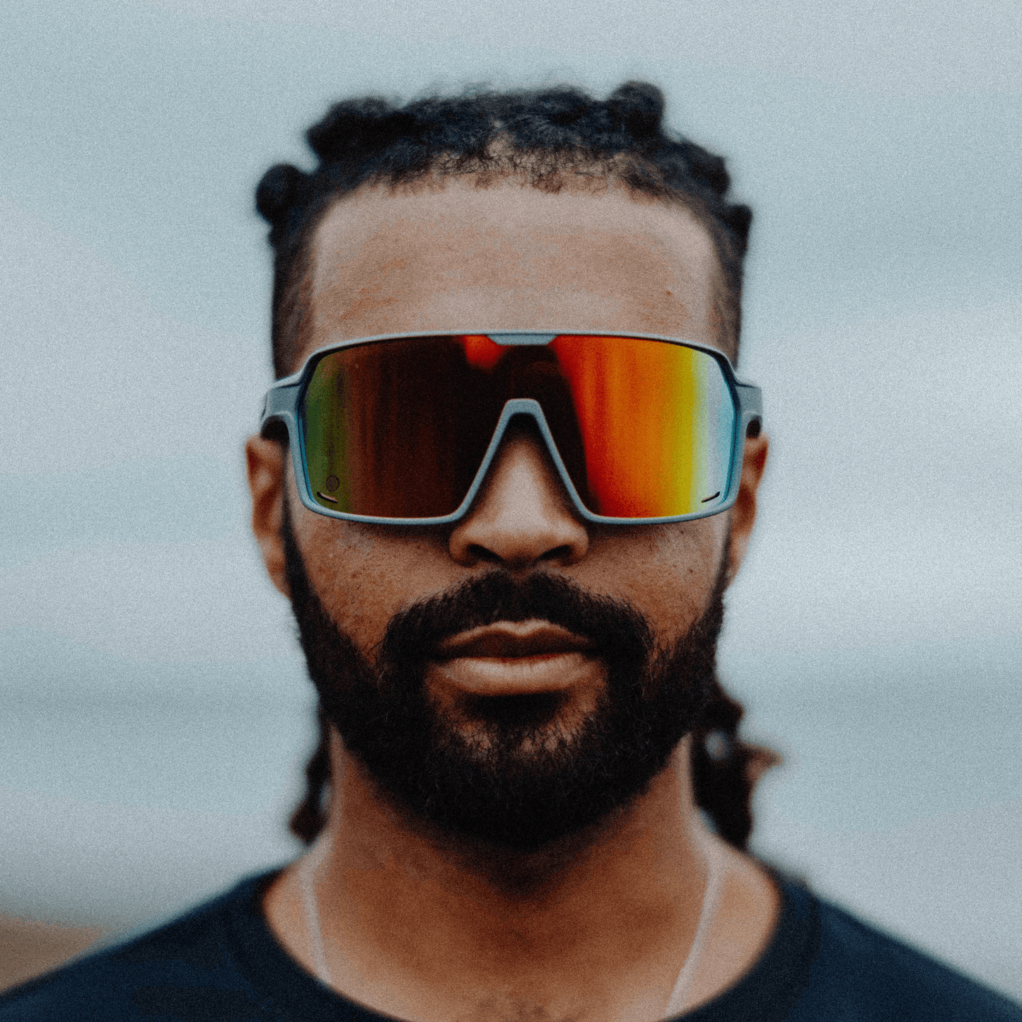 Man wearing Kukuna® Summit lifestyle sunglasses with red mirror lenses and a matte grey frame, showcasing sporty style and performance.