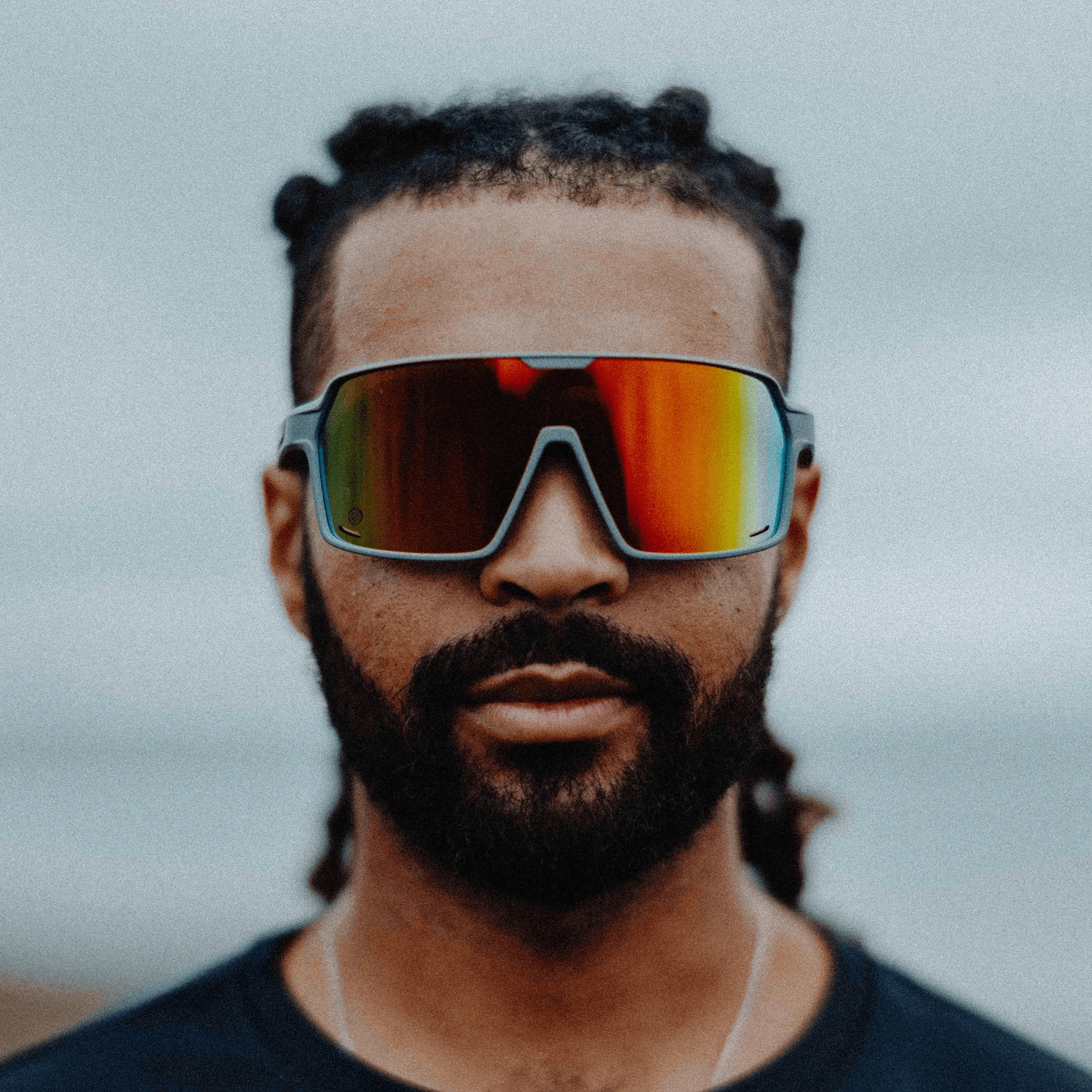 Man wearing Kukuna® Summit lifestyle sunglasses with red mirror lenses and a matte grey frame, showcasing sporty style and performance.