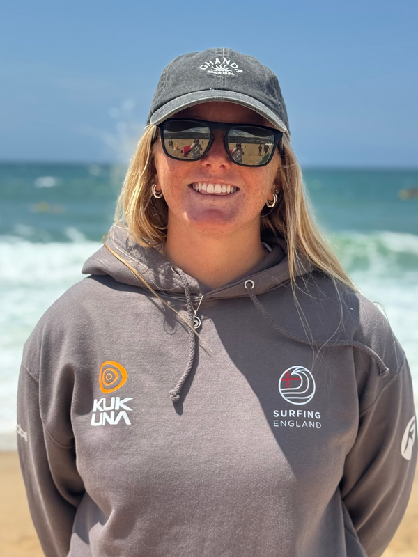 Charlotte Mulley wearing a gray hoodie with kukuna logos on a beach