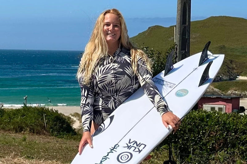 Charlotte Mulley holding a surfboard with a scenic ocean view in the background