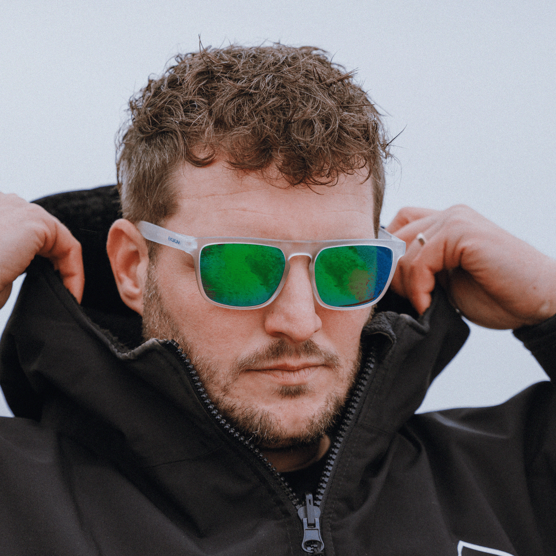 male surfer wearing  Kukuna Barricane polarised sunglasses with clear frosted frame and green mirror lenses