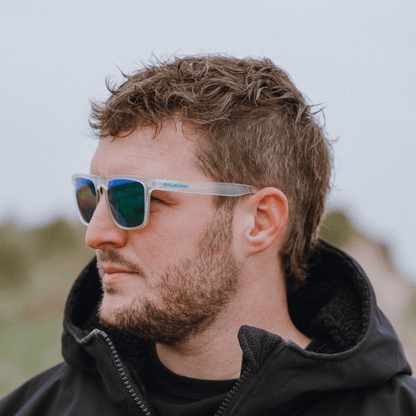male surfer wearing  Kukuna Barricane polarised sunglasses with clear frosted frame and green mirror lenses